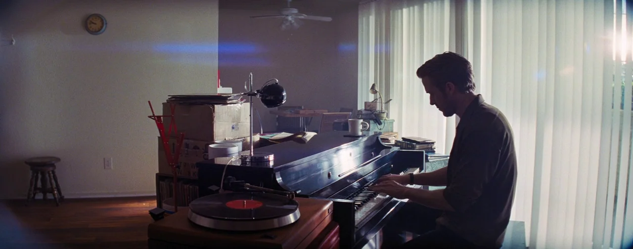La La Land (2016) movie still: medium — A living space containing a grand piano, cardboard boxes, and a record player.