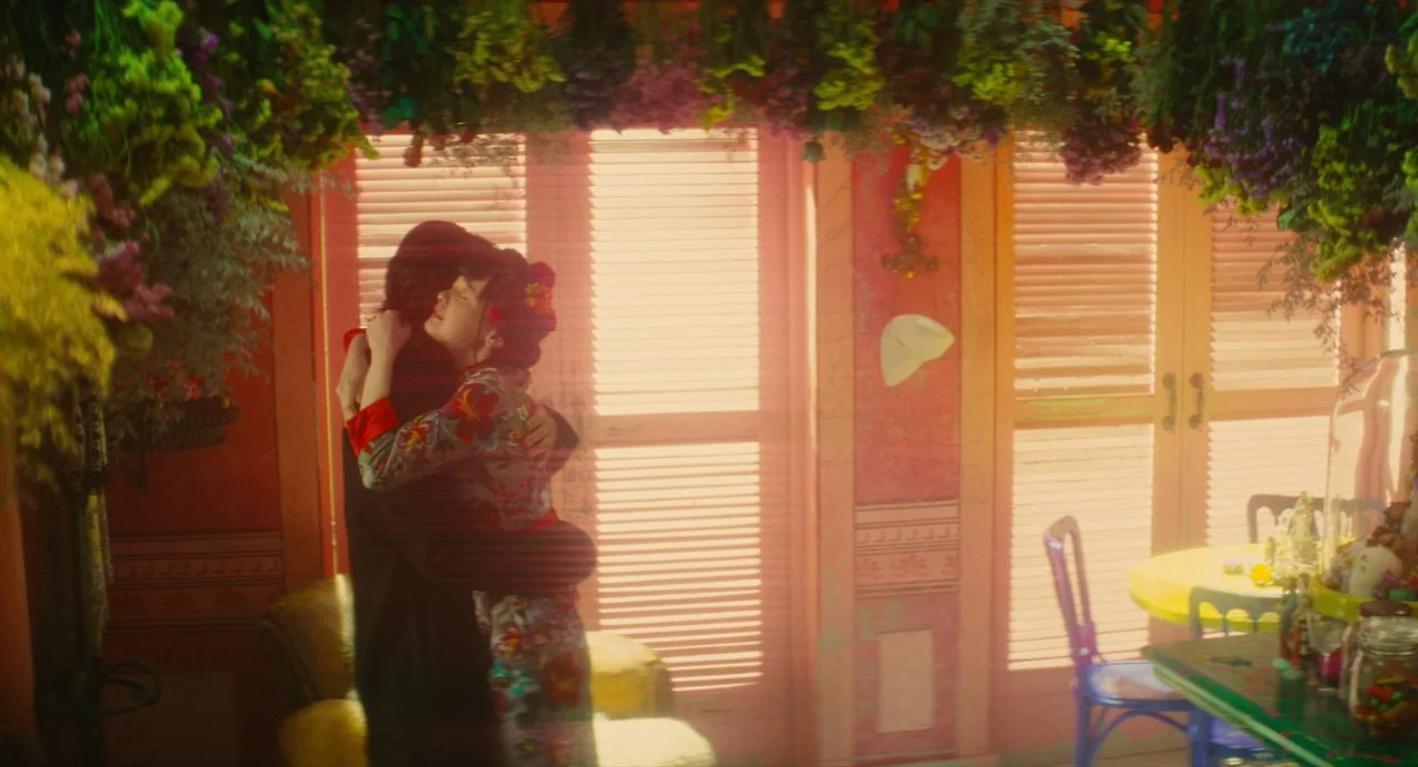 Diner (2019) movie still: medium — An interior space is decorated with clusters of dried flowers hanging from the ceiling. A man and woman embrace…
