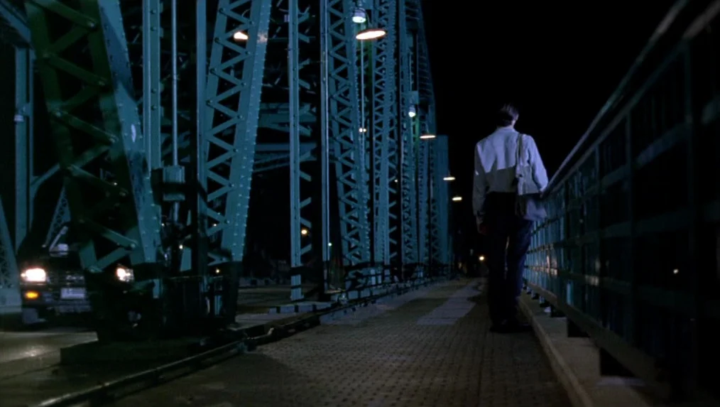 Last Life in the Universe (2003) movie still: fullbody — A steel truss bridge spans the darkness at night with glowing overhead lamps. A solitary…