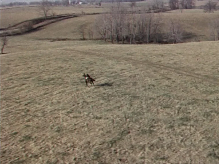 Marnie (1964) movie still: wide — A vast, rolling, dry grassy field extends towards a line of bare trees. A lone rider on a horse moves steadily…