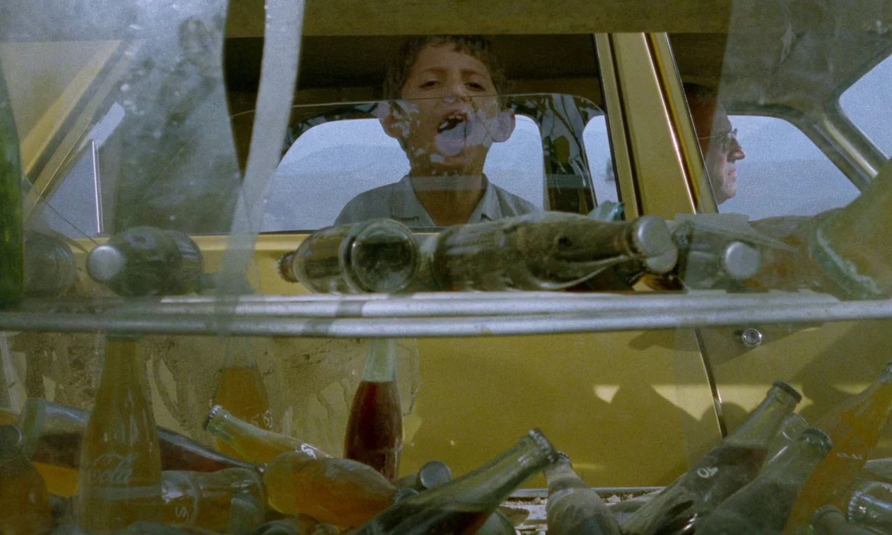 Life, and Nothing More (1992) movie still: medium — A yellow vehicle is filled with glass bottles of various beverages. A young boy looks through a…