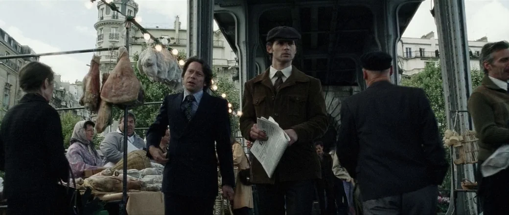 Munich (2005) movie still: medium — A busy outdoor market set underneath a massive steel bridge structure in Paris. Men in period clothing walk past…