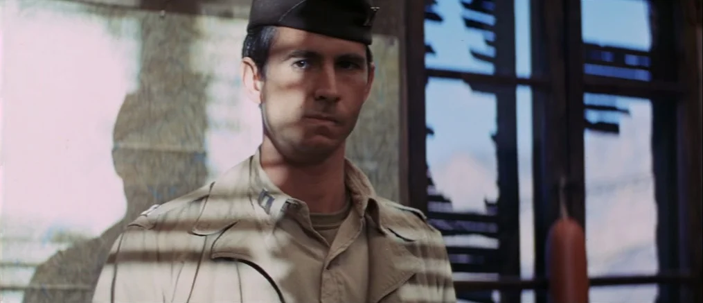 Catch 22 (1970) movie still: medium — A man in a military uniform stands indoors behind slats casting horizontal shadows. Through the window, the…