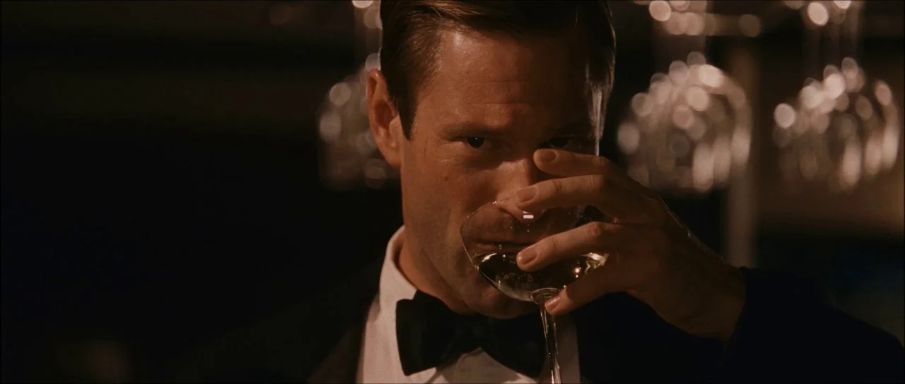 The Black Dahlia (2006) movie still: closeup — A dimly lit bar with out-of-focus glassware hanging in the background. A man in formal wear drinks…