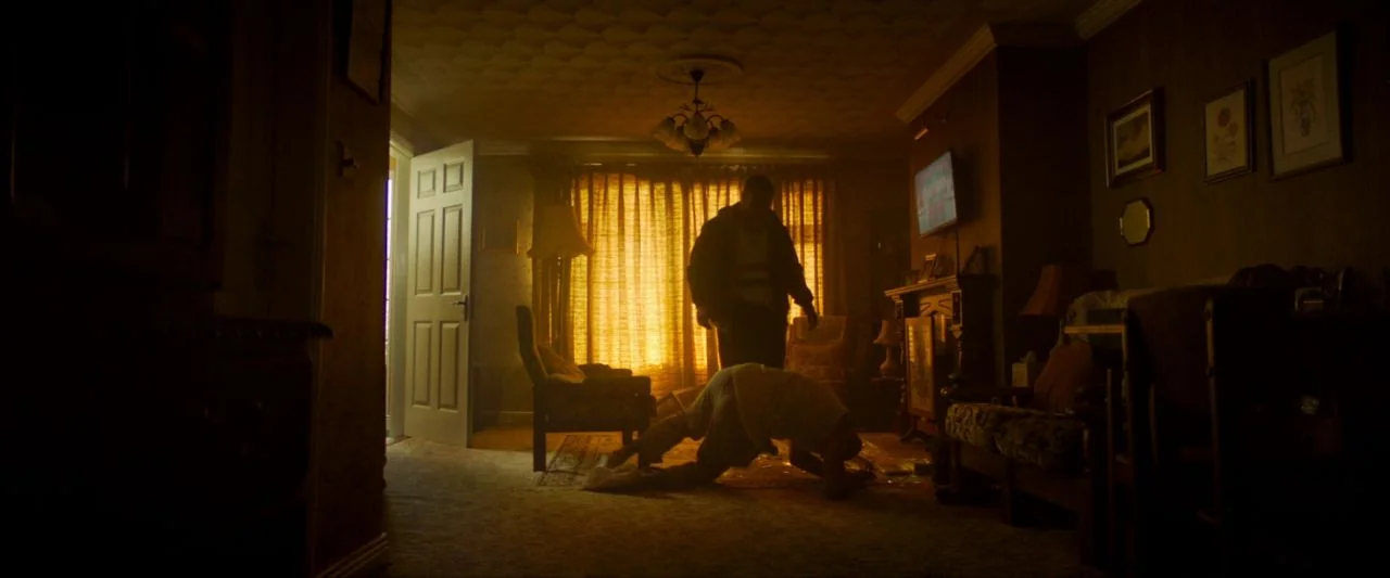 Calm With Horses (2019) movie still: wide — A cluttered suburban living room is illuminated by intense sunlight streaming through drawn curtains.…