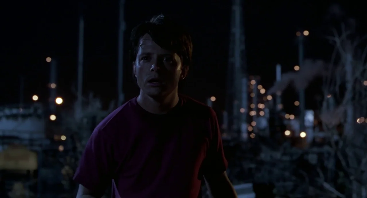 Back to the Future II (1989) movie still: medium — An industrial landscape at night with illuminated structures visible in the blurry background. A…