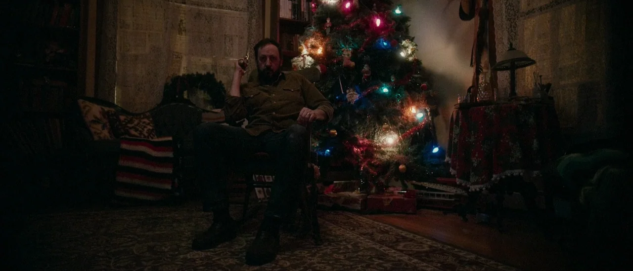 I Trapped The Devil (2019) movie still: medium — A dimly lit room features a decorated Christmas tree with multicolored lights beside a rocking…