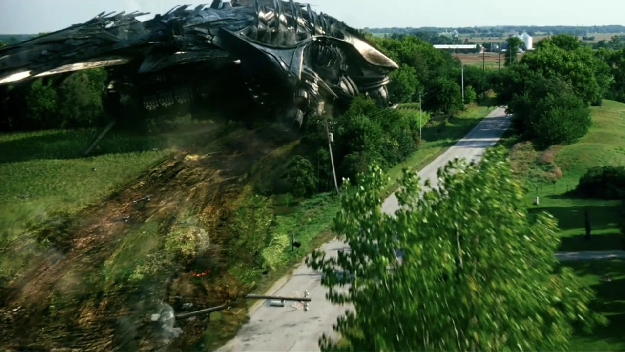 Transformers: Age of Extinction (2014) movie still: wide — A rural landscape features a paved road running through green trees and fields. A large…