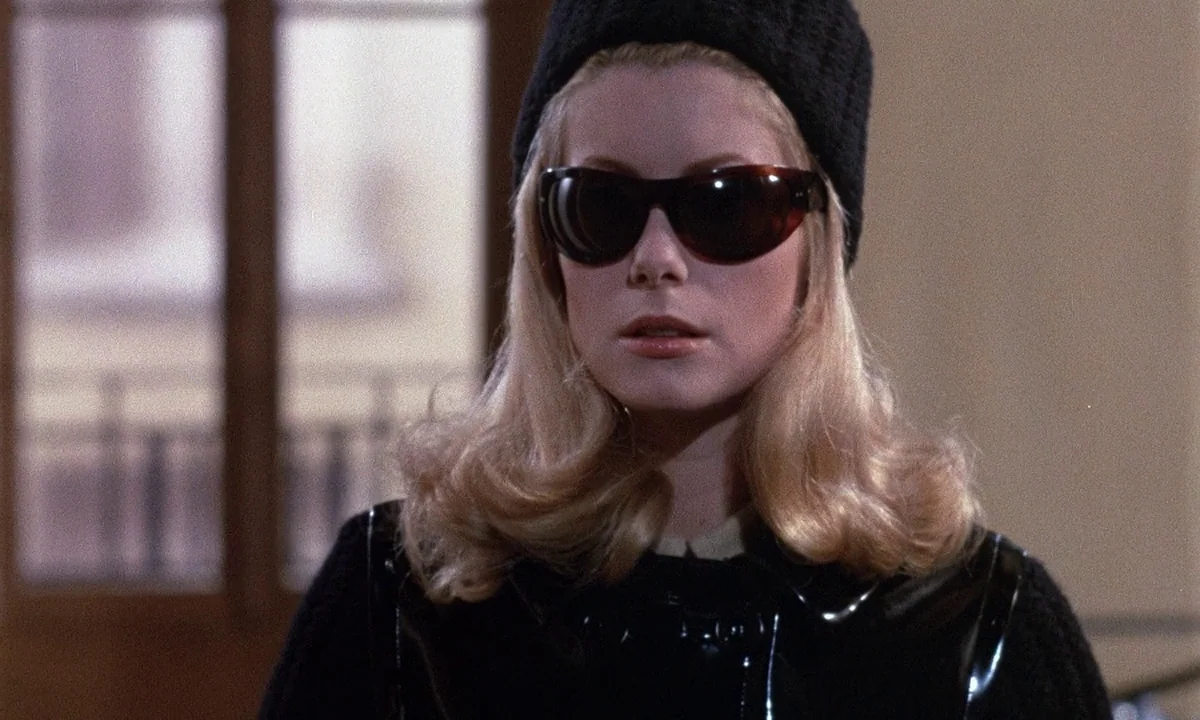 Belle De Jour (1967) movie still: closeup — A bright indoor space features a blurred doorway visible in the background. A young woman with blonde…