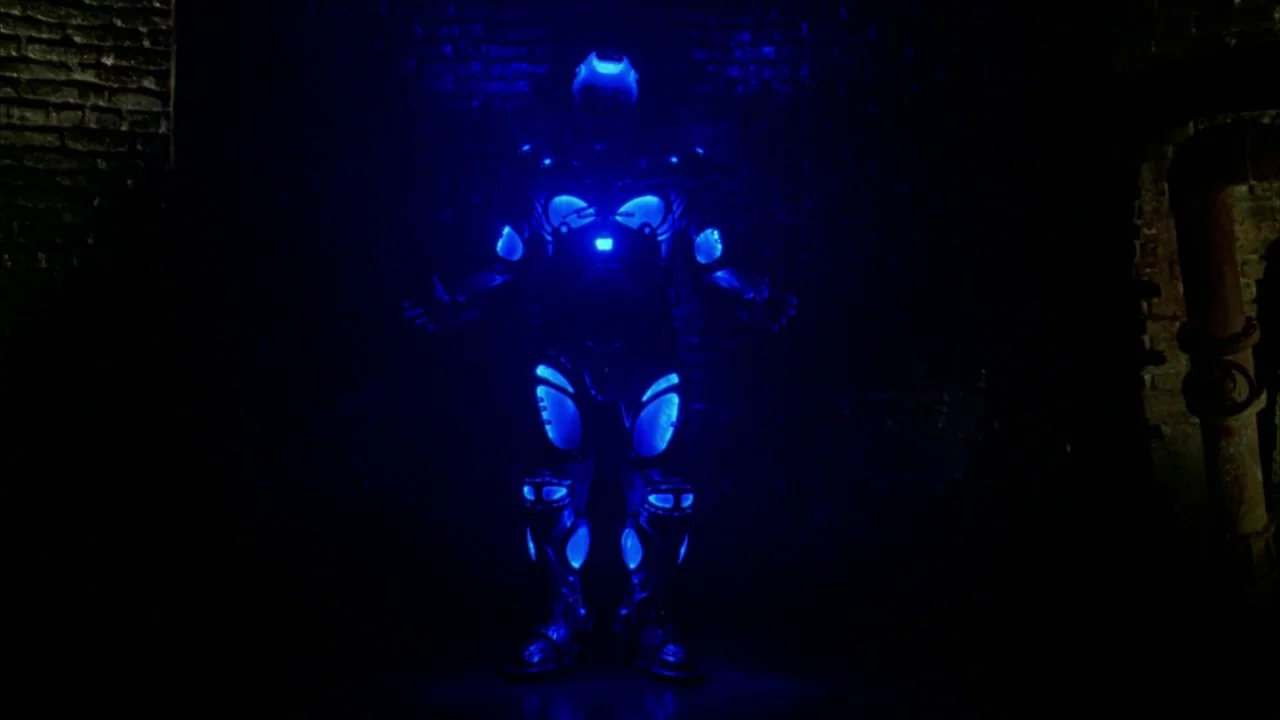 Batman & Robin (1997) movie still: fullbody — A dark, textured brick wall serves as the backdrop for a central illuminated figure. A person wearing…