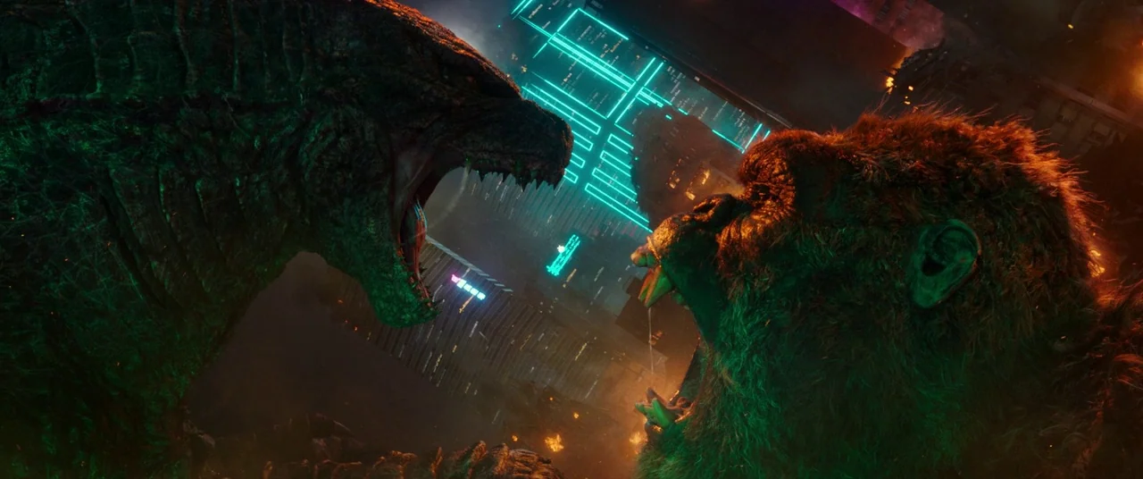 Godzilla Vs. Kong (2021) movie still: medium — A night time city street features two massive monsters roaring at each other closely. Neon buildings…