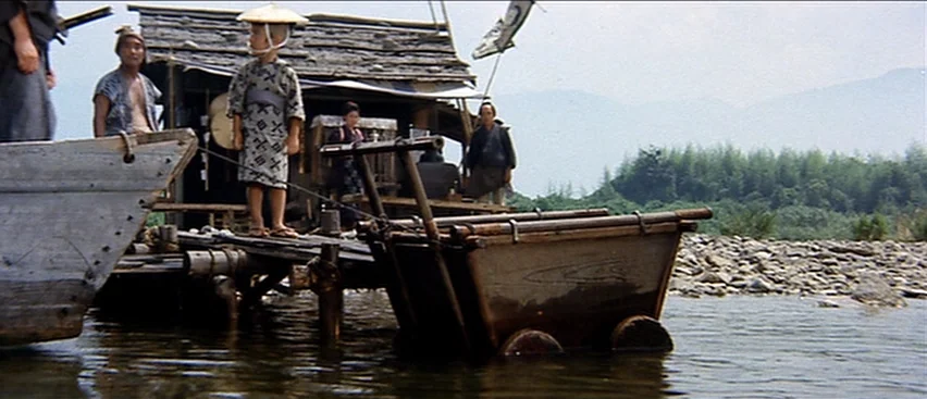 Lone Wolf and Cub: Baby Cart to Hades (1972) movie still: wide — A wooden dock extends into a shallow rocky river near a rural settlement. A young…