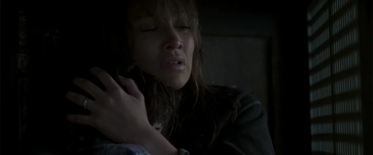 Enough (2002) movie still: closeup — A dark indoor space contains a person holding a small figure closely. The woman embraces the child against her…