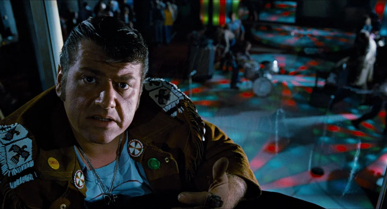 Phantom of the Paradise (1974) movie still: medium — A man in a fringed suede jacket sits under colorful spinning lights in a disco. He stares…
