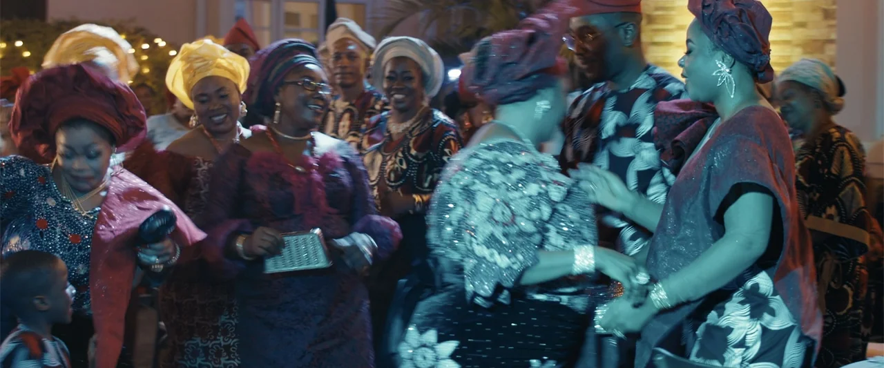 Big Love (2012) movie still: medium — A festive outdoor social gathering with many people in formal traditional attire. Guests are laughing and…
