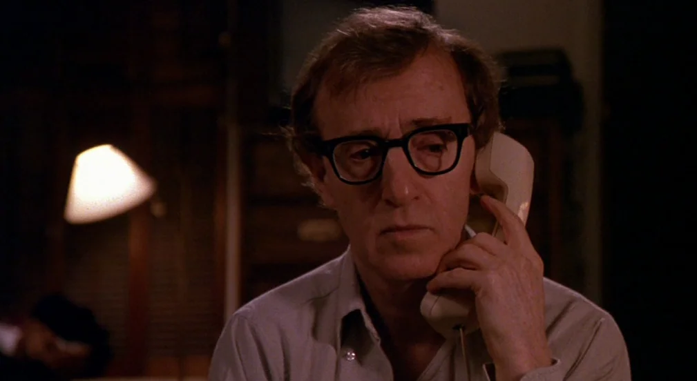 Crimes and Misdemeanors (1989) movie still: closeup — A dark indoor setting features a person holding a telephone receiver against their ear. The…