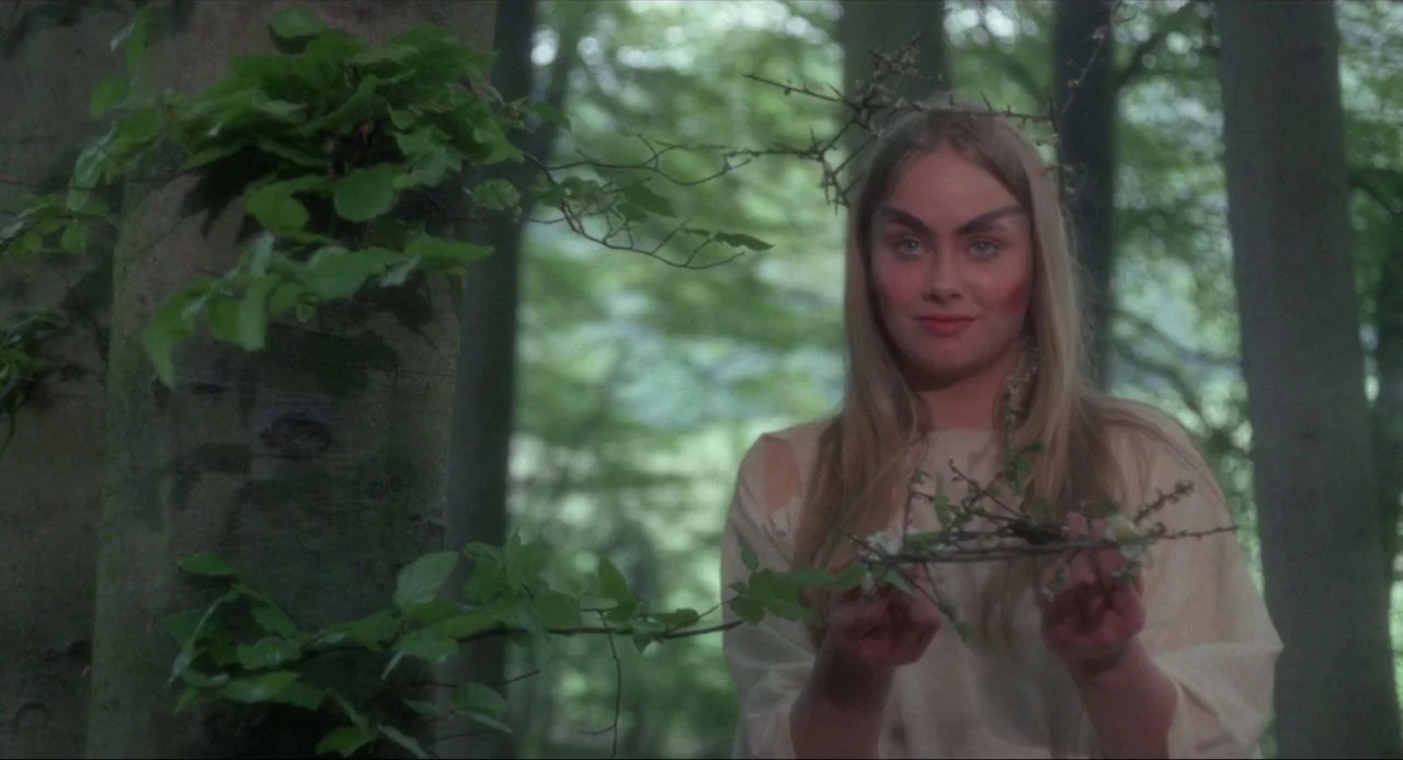 The Blood on Satan’s Claw (1971) movie still: medium — A dense woodland setting featuring mature trees with lush green leaves. A woman stands…