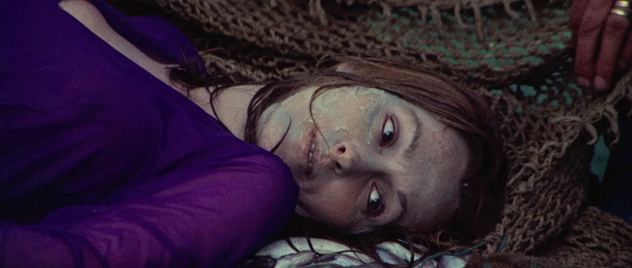 Death Walks On High Heels (1971) movie still: closeup — A woman lies on a coarse, tangled brown fishing net outdoors. She is positioned on the…