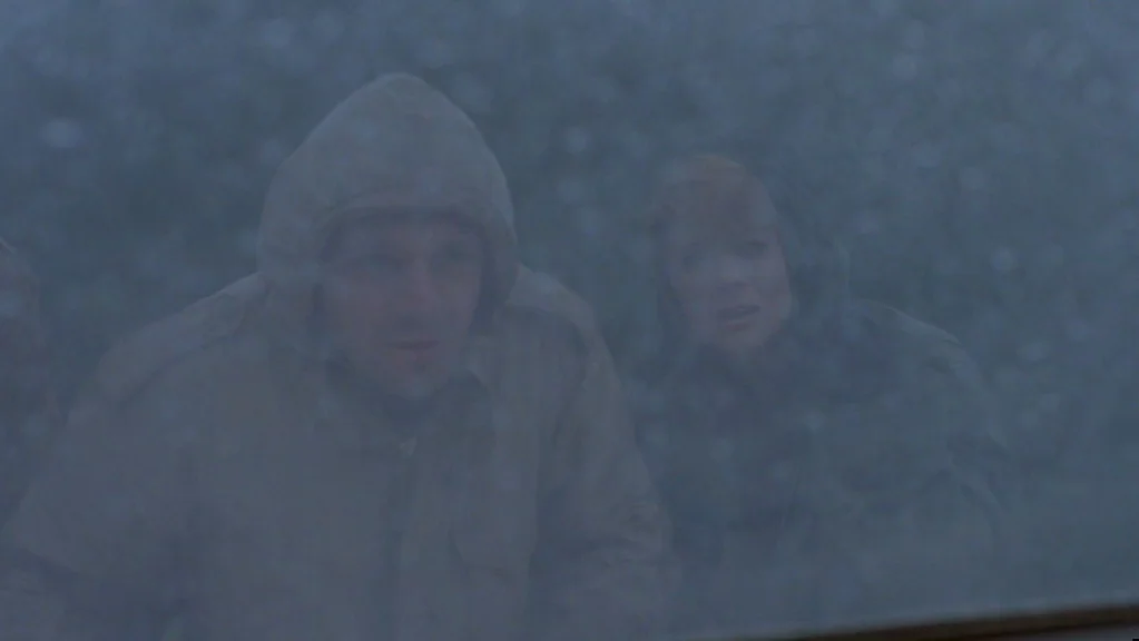 Magic (1978) movie still: medium — A man and a woman stand outside, peering through a heavily rain-covered glass window pane. The dark, obscured…