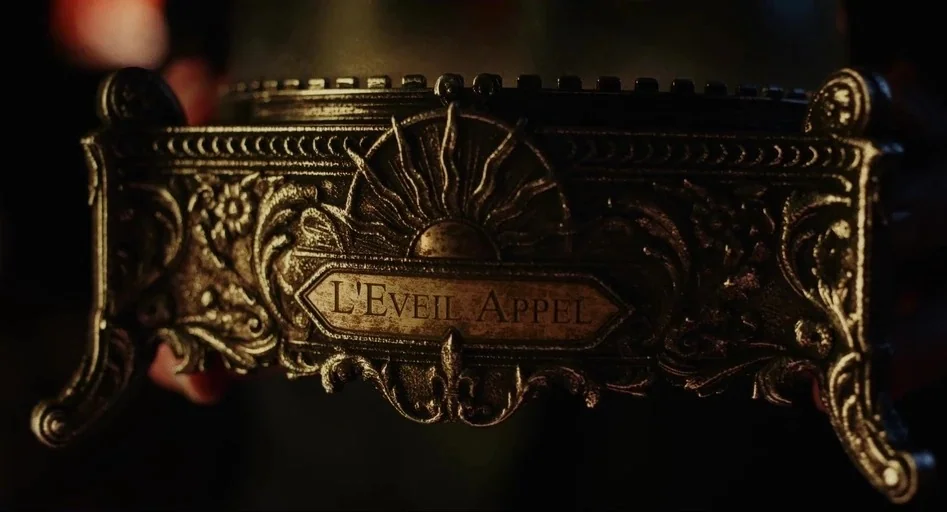 Wake Up Dead Man (2025) movie still: closeup — A dark, ornate metallic box base features intricate scrollwork and a central sun motif. The words…