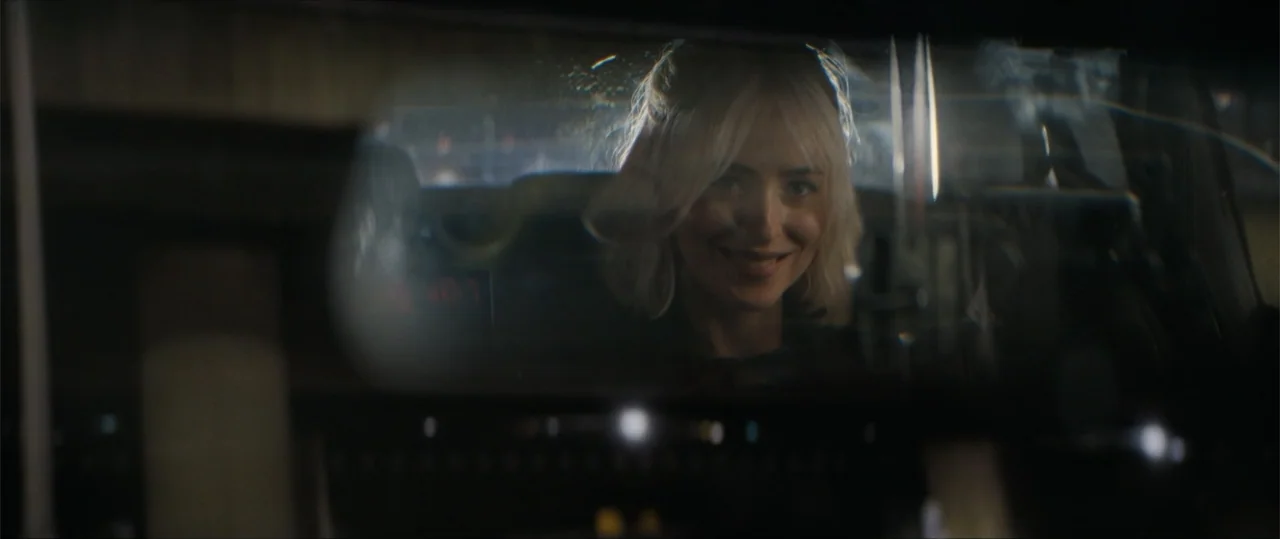 Daddio (2024) movie still: closeup — A view through a car's rearview mirror shows a young woman sitting inside. The subject looks into the mirror…