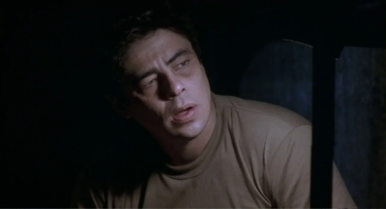 The Hunted (2003) movie still: closeup — A dark, sparsely detailed interior space is illuminated by a single directional light source. A man in a…