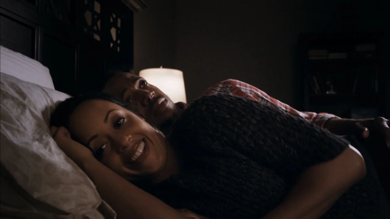 A Haunted House (2013) movie still: medium — A dark, dimly lit bedroom at night with a headboard visible behind the couple. A woman and a man lie…