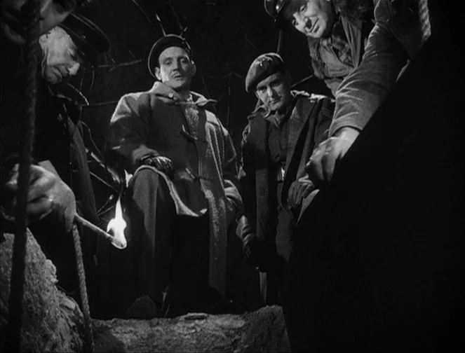 The Third Man (1949) movie still: medium — A dark subterranean enclosure with dirt walls and rough textures. Four men gather around an opening in…