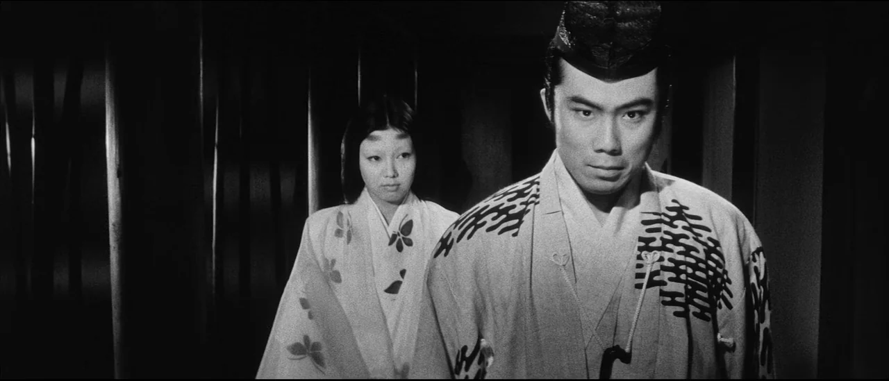 Kuroneko (1968) movie still: medium — A dimly lit interior hallway with dark wooden slats and shadows lining the walls. A man and a woman in…