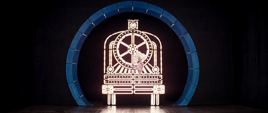 The Boy Friend (1971) movie still: wide — A dark, empty performance area features a large neon locomotive outline centered inside an arch. A single…