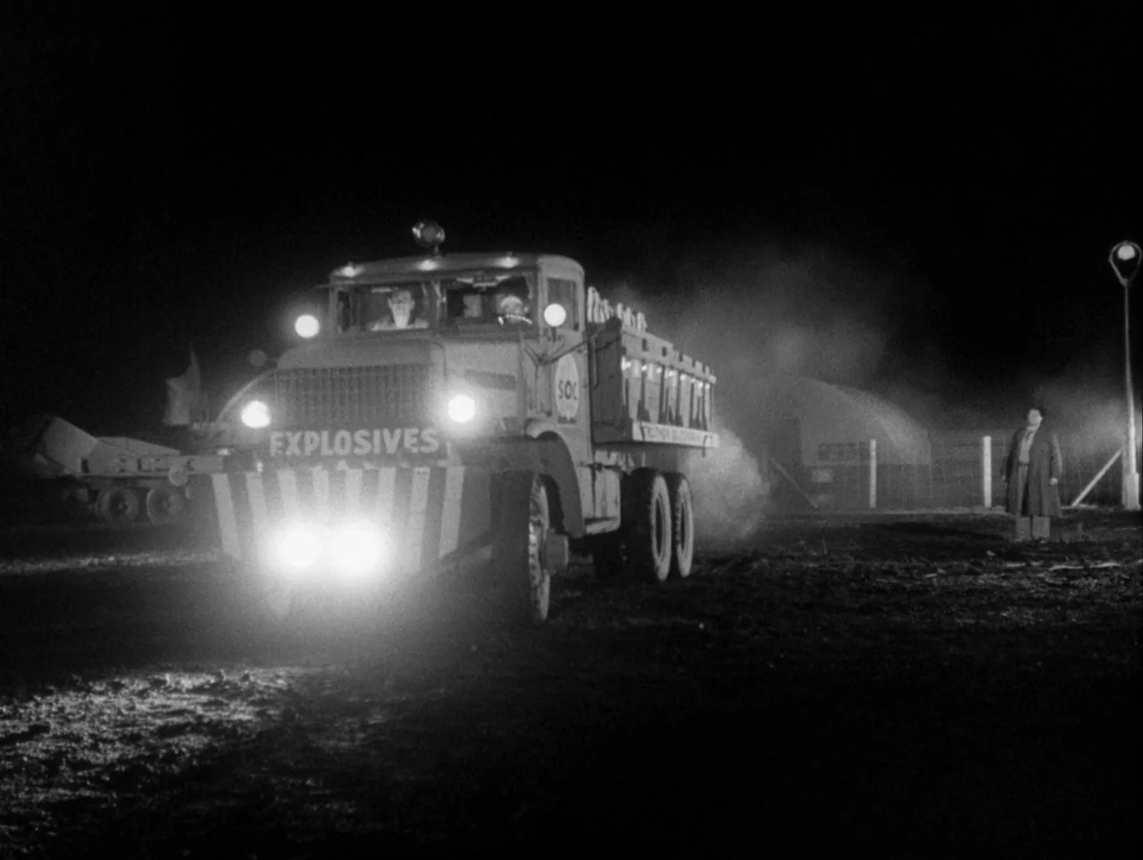 The Wages of Fear (1953) movie still: wide — A heavy truck marked EXPLOSIVES drives through a dark, desolate, and muddy industrial field. The bright…