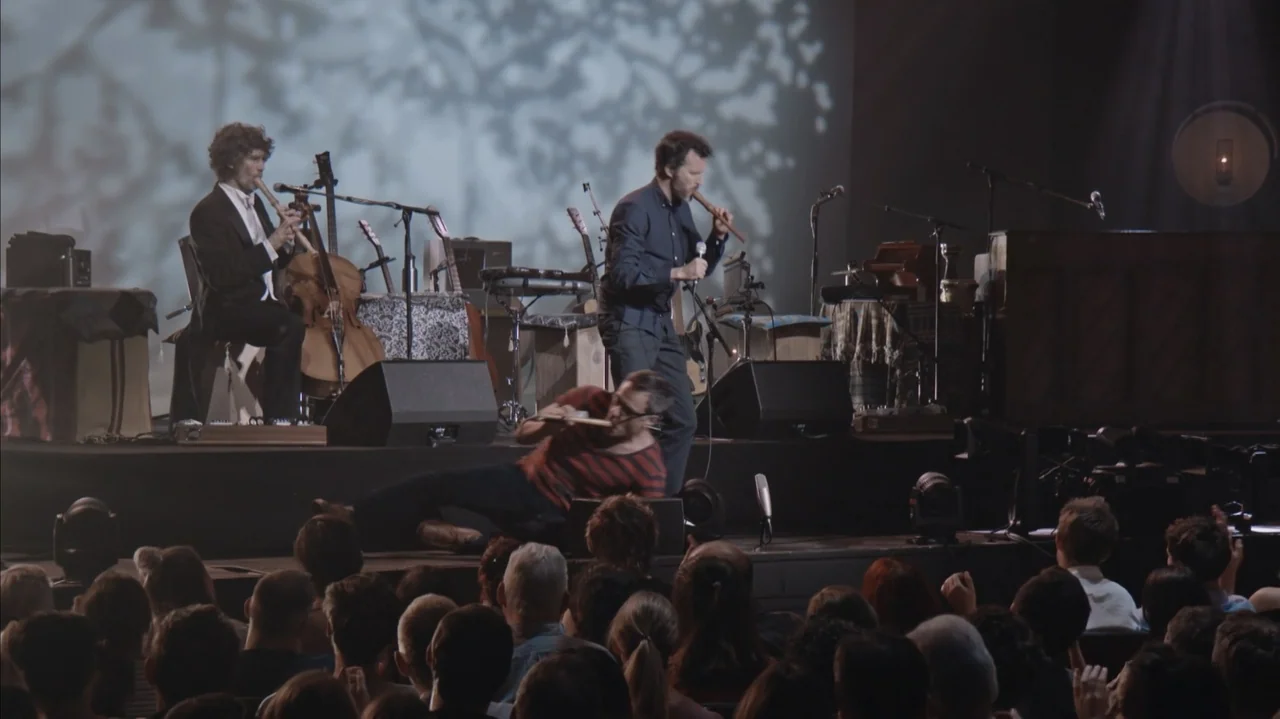 Flight of the Conchords: Live in London (2018) movie still: medium — A live concert stage features three musicians performing with acoustic…