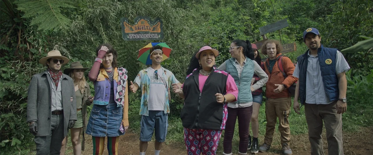 Mirreyes contra Godínez 2: El retiro (2022) movie still: wide — A diverse group of people stands in a dense tropical forest near wooden signs. They…