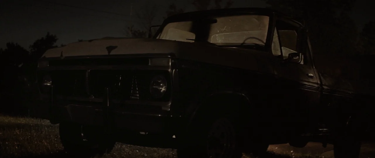 The Strangers: Prey at Night (2018) movie still: medium — An old, dark pickup truck sits on a dirt surface at night. It is silhouetted against a…