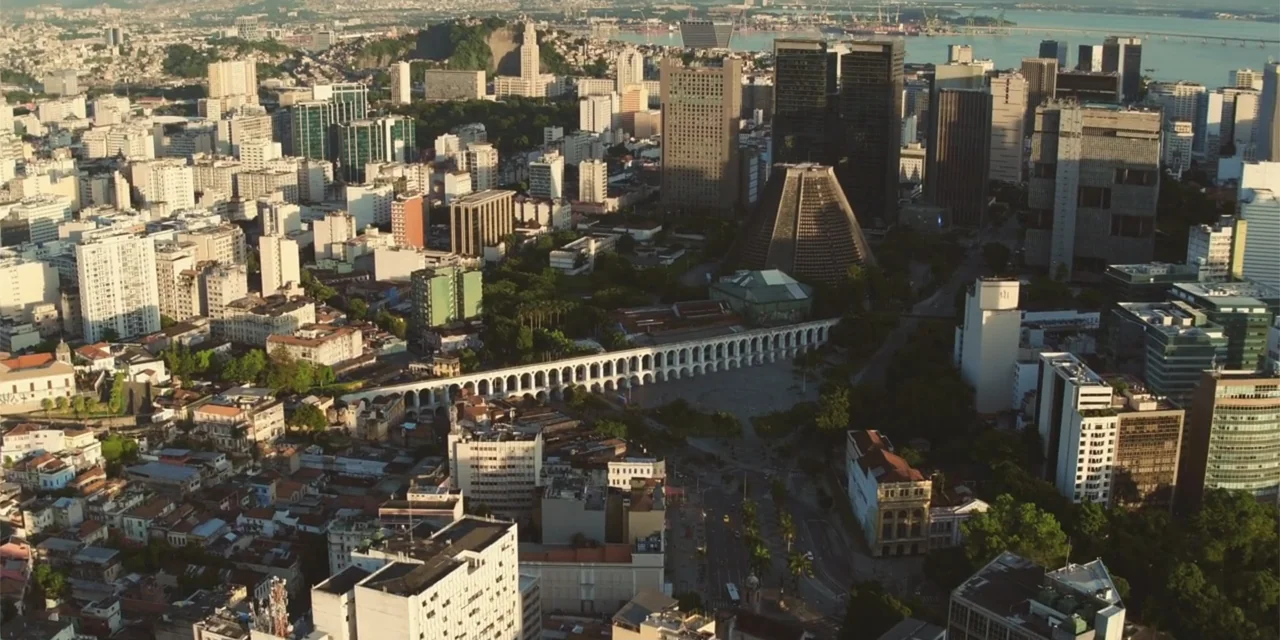 An Unforgettable Year - Summer (2023) movie still: establishing — An aerial view of the Rio de Janeiro city skyline during golden hour. Dense urban…