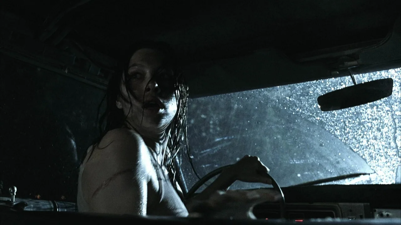 The Texas Chainsaw Massacre (2003) movie still: medium — The interior of a car at night featuring a rain-covered windshield and side window. A woman…