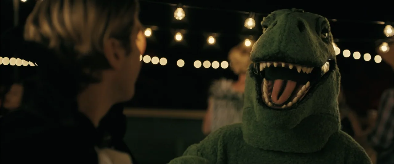 Companion (2025) movie still: medium — An outdoor night party is decorated with rows of illuminated glowing string lights. A person wearing a plush…