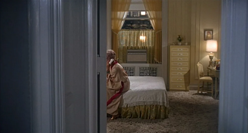 Rosemary’s Baby (1968) movie still: wide — A hotel room features shag carpeting, yellow curtains, and a matching chest of drawers. A woman in a robe…