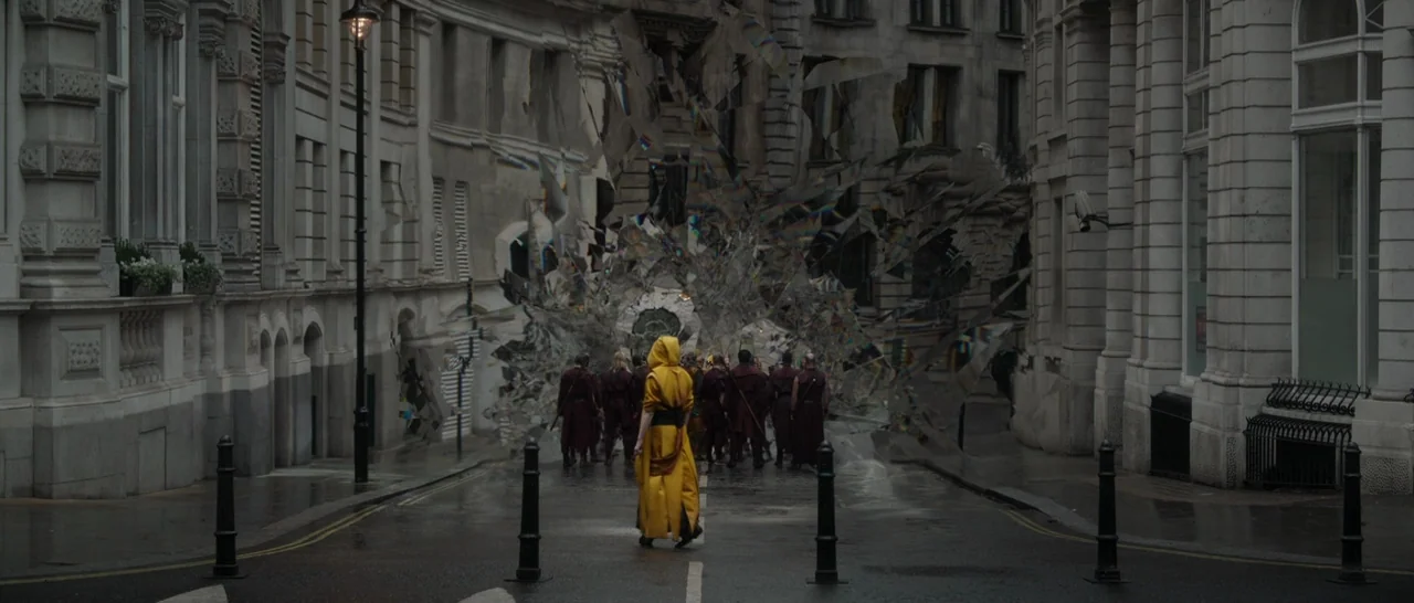 Doctor Strange (2016) movie still: wide — A narrow London street features Victorian-style stone architecture and wet asphalt ground surface. A group…