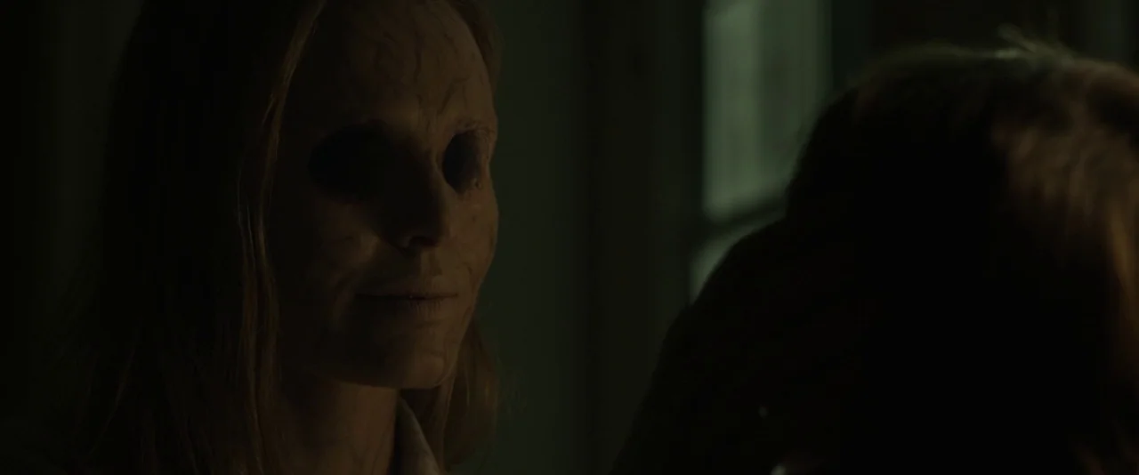 Before I Wake (2016) movie still: closeup — A dimly lit, dark space serves as the backdrop for a distorted encounter. A woman with hollow black eyes…