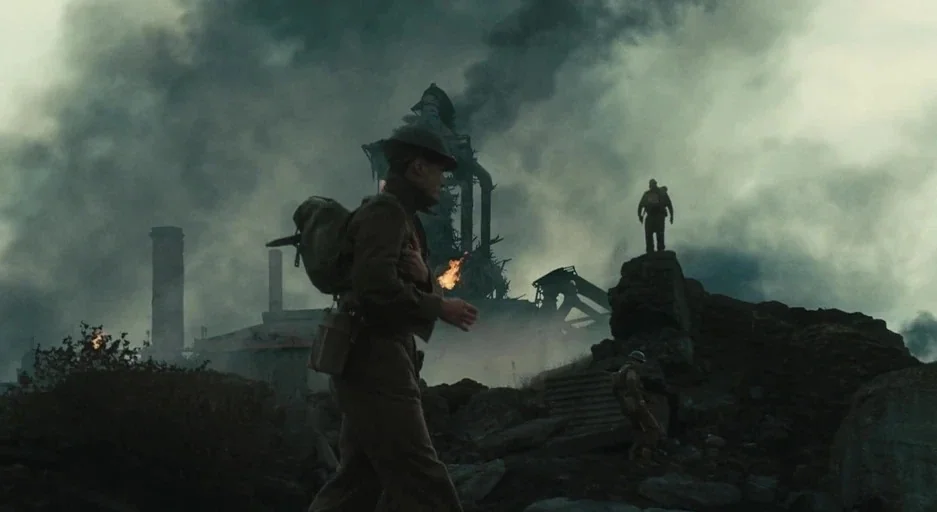 Atonement (2007) movie still: wide — A rocky, desolate landscape features industrial ruins shrouded in thick, dark grey smoke. A soldier in uniform…