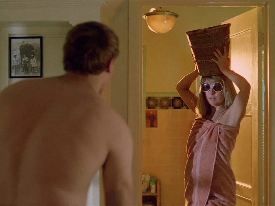One From The Heart (1982) movie still: medium — A woman stands in a doorway wearing a towel and holding a basket. A man stands in the foreground…