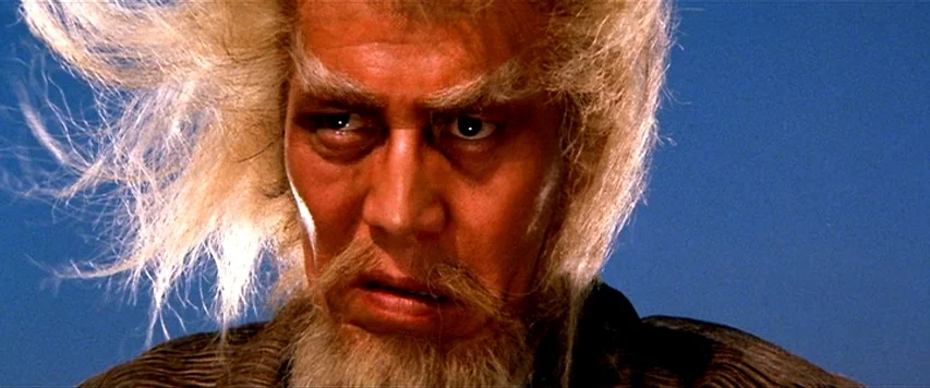 Lone Wolf and Cub: Sword of Vengeance (1972) movie still: closeup — An older man stands outdoors against a clear, solid blue sky background. His…