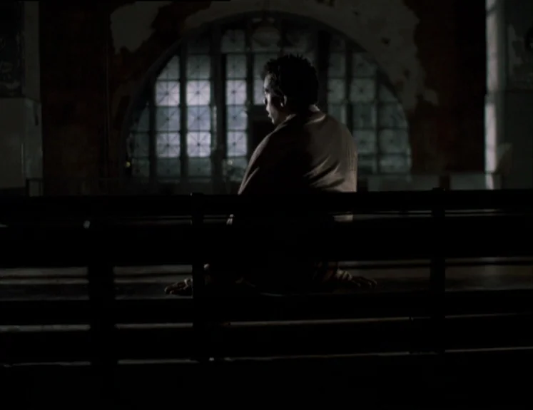 The Brother From Another Planet (1984) movie still: medium — A dimly lit waiting area features a large arched window with a grid pattern. A man sits…