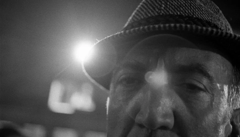 Seconds (1966) movie still: closeup — A dimly lit, high-contrast interior space with dark shadows. An elderly man in a fedora looks toward the…