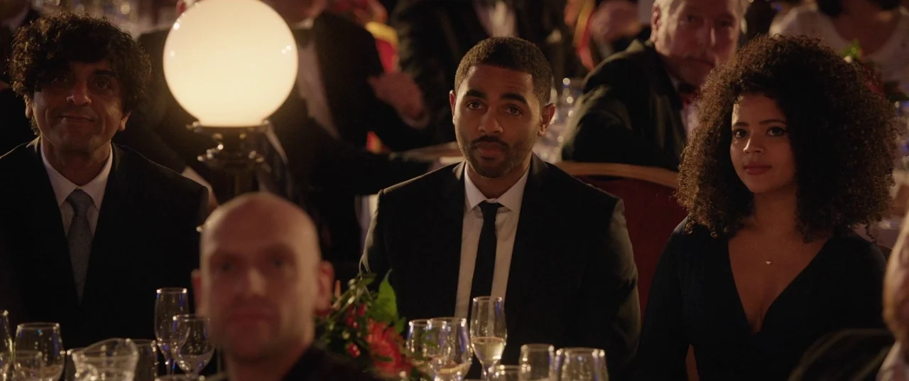 Journeyman (2017) movie still: medium — A banquet hall with multiple tables occupied by people in formal attire. Three individuals in the foreground…