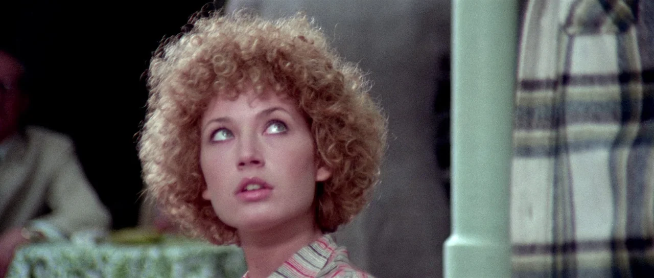 The Suspicious Death of a Minor (1975) movie still: closeup — A woman with blonde curly hair looks upward while sitting outdoors. A pale green…