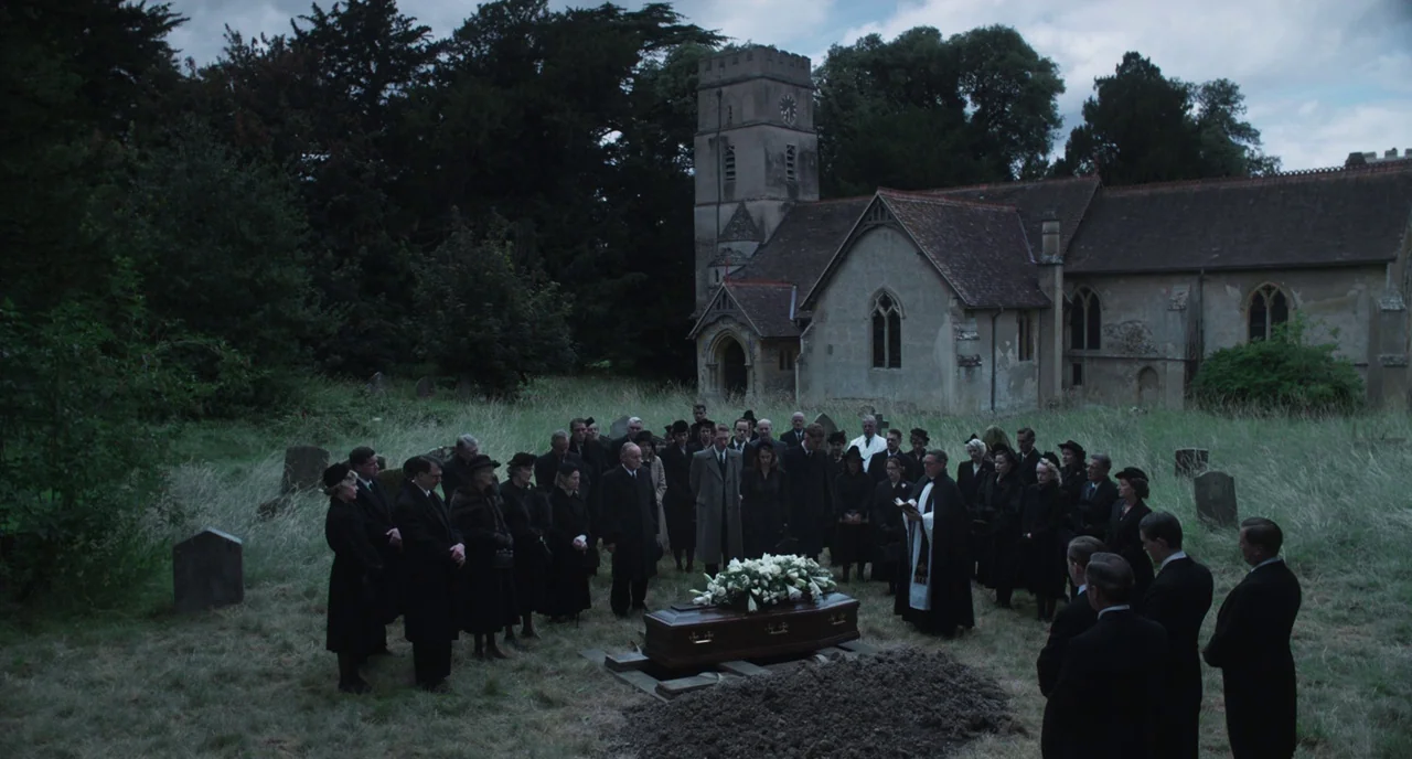 The Little Stranger (2018) movie still: wide — A group of people in mourning attire stand in a circle around a wooden casket. An old stone church…