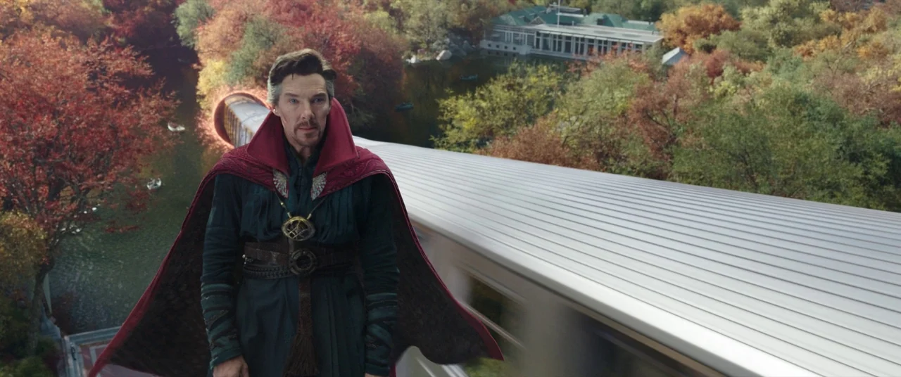 Spider-Man: No Way Home (2021) movie still: medium — A man in magical attire floats above a smooth, elevated metallic track in a park. Autumnal…
