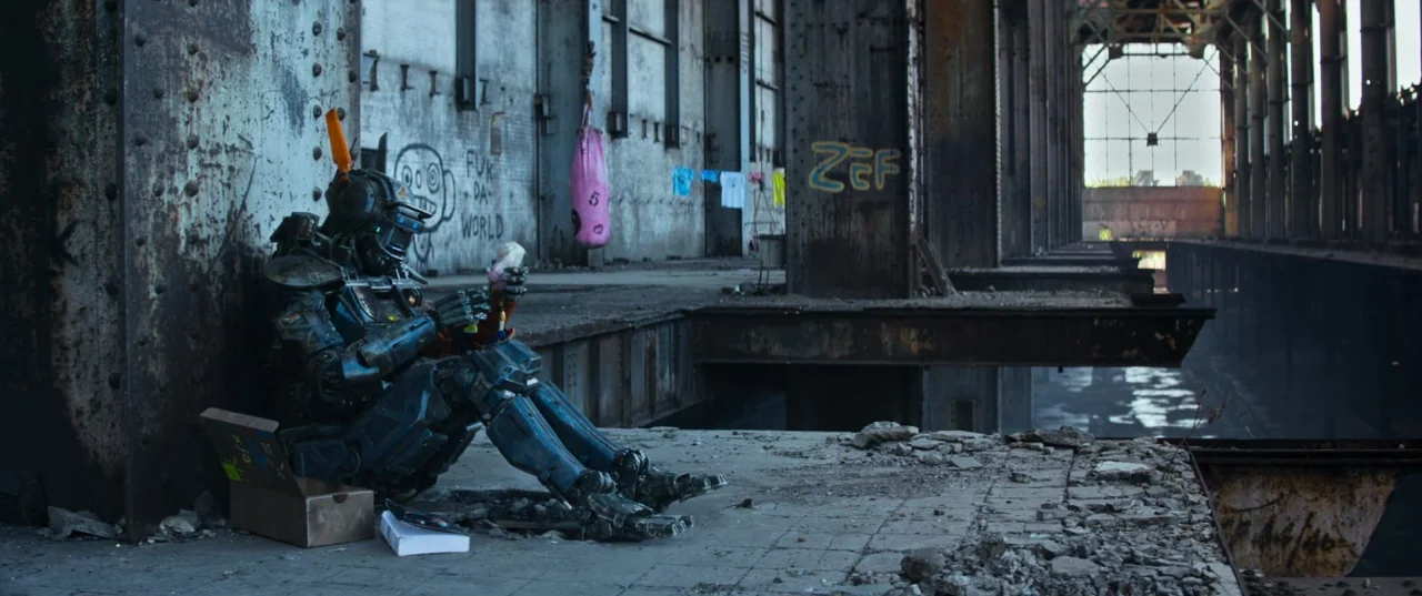 Chappie (2015) movie still: wide — A desolate, industrial interior features rusted steel columns and graffiti against crumbling concrete walls. A…